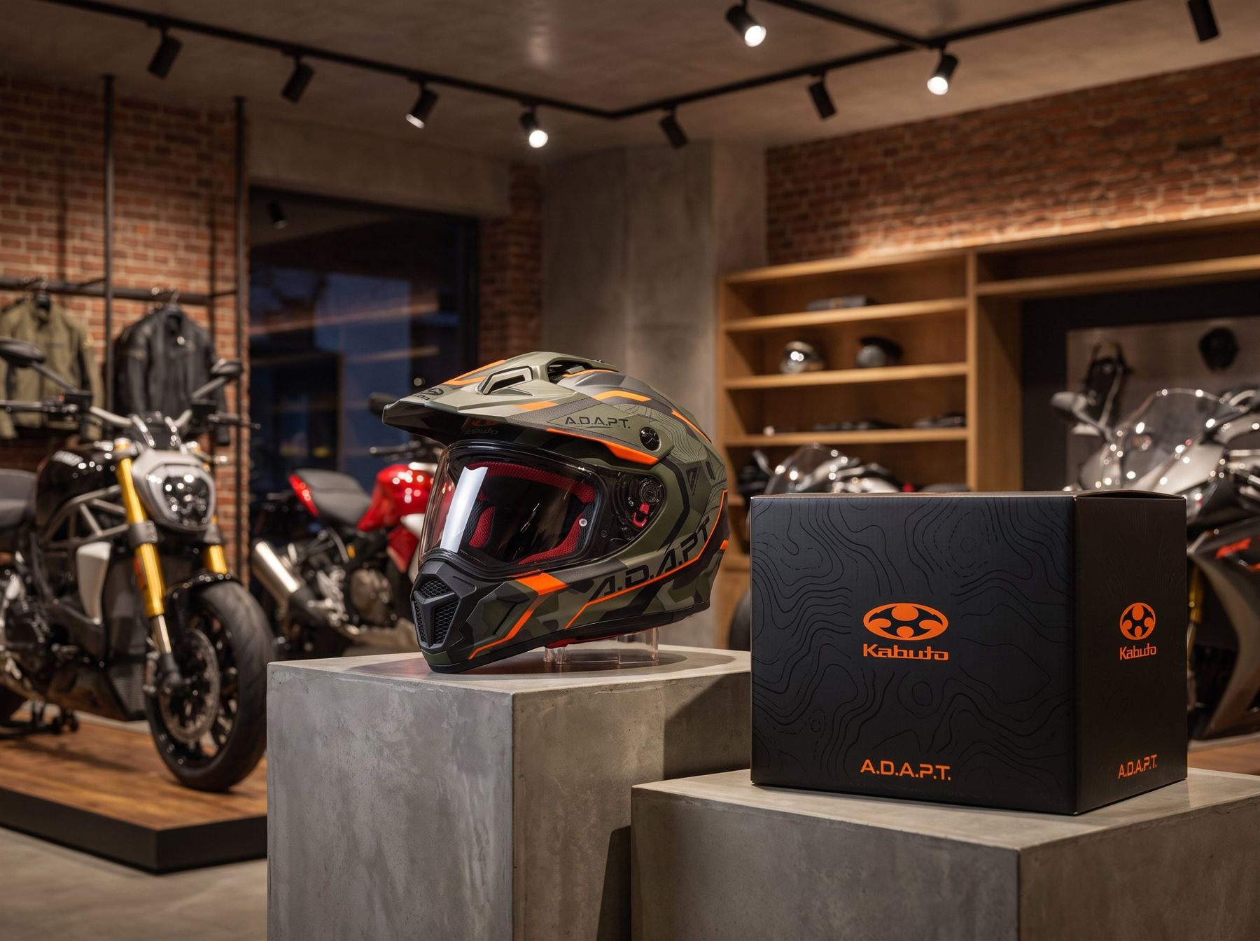 Casque Kabuto A.D.A.P.T. sur un socle en béton à côté de sa boîte noire aux courbes de niveau, dans un showroom moto